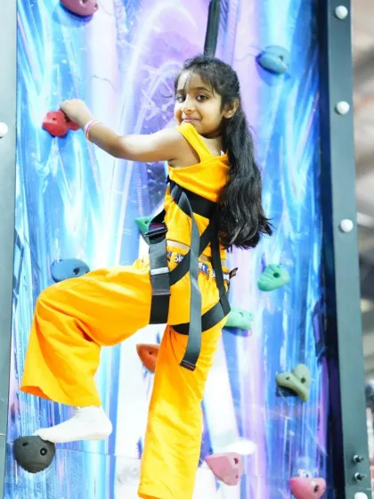 This young adventurer is all smiles as she scales our vibrant climbing wall. Each hold is a step towards the top, making for a rewarding and exciting physical activity.