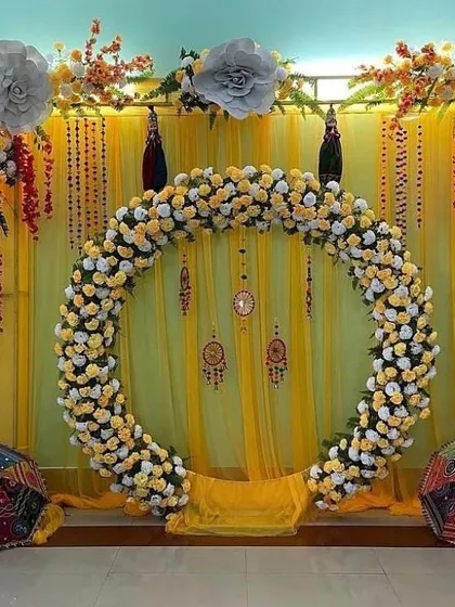 This Haldi decoration features a large circular arch made entirely of yellow and white marigold flowers. Set against a simple yellow drape, this floral ring creates a stunning focal point for ceremony photos.