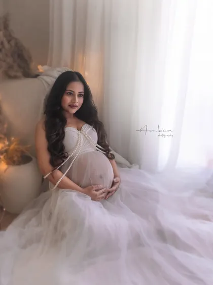 A pretty and ethereal portrait in a light-filled studio setting. The sheer white gown and pearl details create a soft, angelic look, perfect for a dreamy maternity session.
