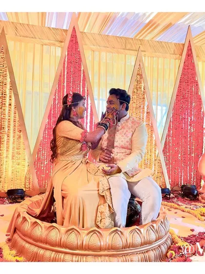 A happy moment from the Haldi ceremony, with the couple seated inside a custom-designed lotus-shaped seat. The backdrop features geometric panels filled with marigold flowers.