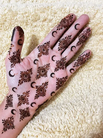 A playful geometric design with repeating sun and moon motifs across the palm and fingers.