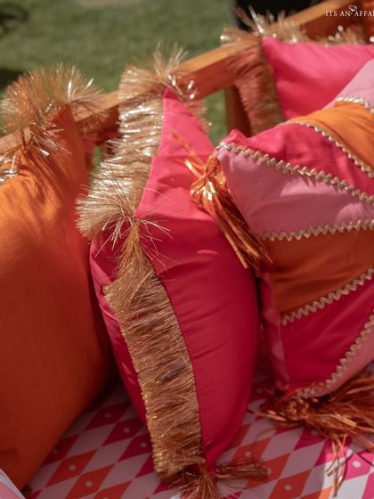 A close-up of the custom cushions, featuring vibrant pink and orange fabrics with gold fringe and gota patti work, reflecting the fun and festive theme.