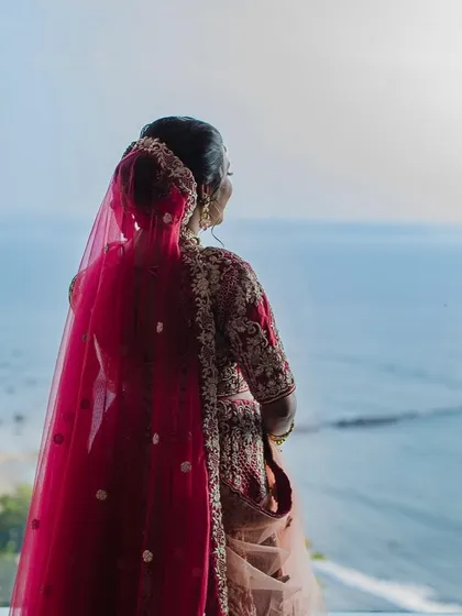 A silhouette shot of the bride looking out at the sea. The elegant floral bun and the drape of her dupatta are highlighted, showcasing the importance of details in the overall bridal look.