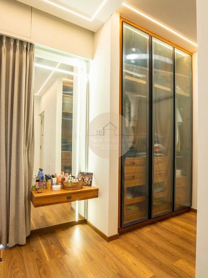 This walk-in closet area features a fluted glass wardrobe that offers a glimpse of the contents while keeping them dust-free. Paired with a floating dressing table and backlit mirror, it creates a dedicated and elegant space for getting ready.