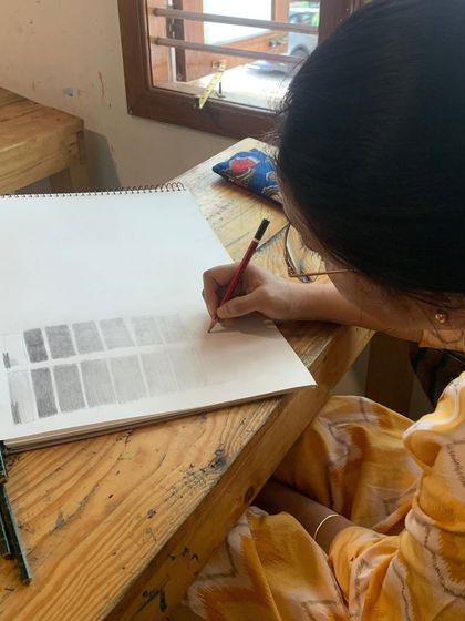 A student practices creating value scales with a pencil. This fundamental exercise teaches control over pressure and tone, which is crucial for realistic shading.