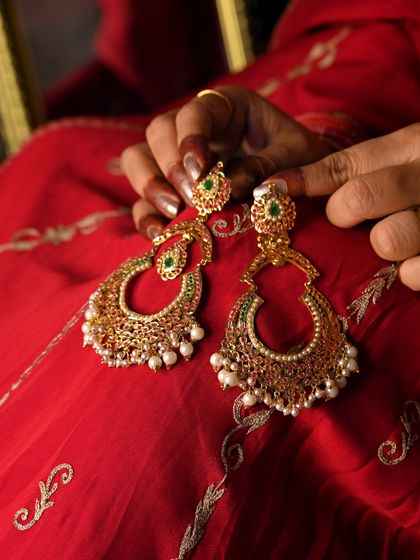 A beautiful shot of the 'मणिकर्णिका' (Manikarnika) earrings, held in hand against a traditional red outfit.