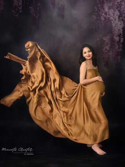 A dynamic and artistic fabric toss. The golden silk flows beautifully around the mom-to-be, creating a sense of weightlessness and grace.