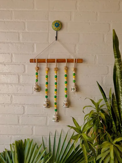 Our 'Beads and Bells' handmade wall hanging in the 'Laburnum' variant, with yellow and green beads. This 26-inch piece comes with a ceramic wall hook and is perfect for adding a touch of color to your home.