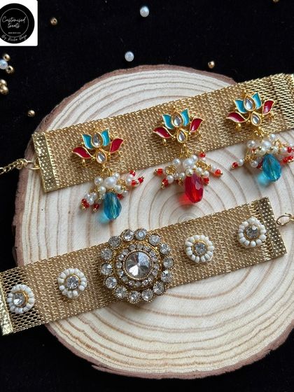 A modern take on the Bhaiya-Bhabhi set, featuring a wide mesh band. The top rakhi has colorful hanging beads, while the bottom one has a classic stone centerpiece.