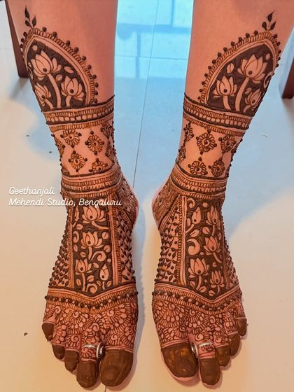 Full coverage leg mehendi for a baby shower. The design features intricate lotus patterns and jaal work, extending up the shins for a grand look.