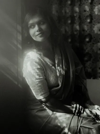 A classic black and white window-lit portrait. The play of light and shadow across the model's face and clothing creates a timeless, cinematic feel, full of quiet contemplation.