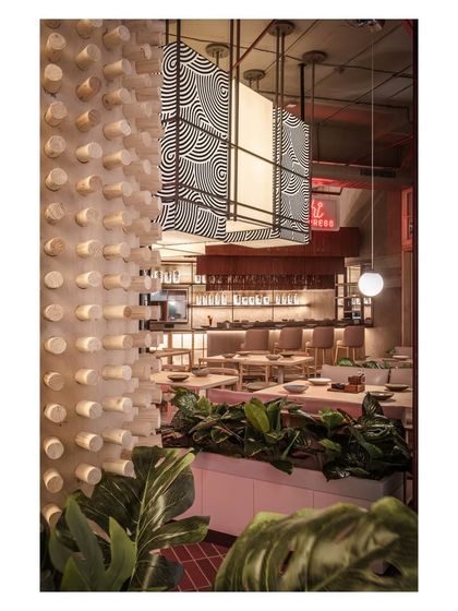 A textured wooden dowel wall adds a unique tactile element to the space, contrasting with the sleek bar and lush plants. This detail demonstrates our focus on materiality to create a rich sensory experience.