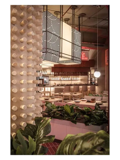 A textured wooden dowel wall adds a unique tactile element to the space, contrasting with the sleek bar and lush plants. This detail demonstrates our focus on materiality to create a rich sensory experience.