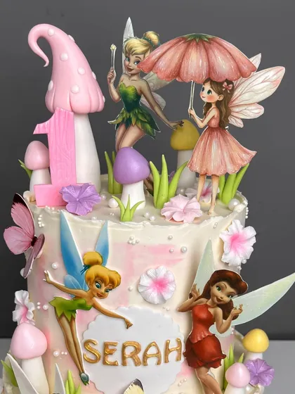 The top tier of our fairy house cake, featuring a large pink mushroom, the number '1' for a first birthday, and beautifully detailed fairy toppers, including one holding a tiny umbrella.