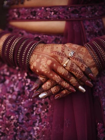 A close-up of the stained hands against a beautiful purple lehenga. The color contrast is striking and elegant.