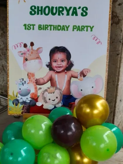 A personalized welcome sign for a jungle-themed first birthday party. The sign features a photo of the birthday boy, cute animal graphics, and a small balloon arrangement at the base.