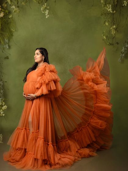 A graceful side profile of a mom-to-be, with the orange gown's train fanned out for a dramatic effect.