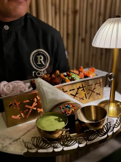 A server presents a personalized platter of tikkas with mint chutney and pickled onions. This individual serving style is perfect for passed appetizers at a sophisticated event.