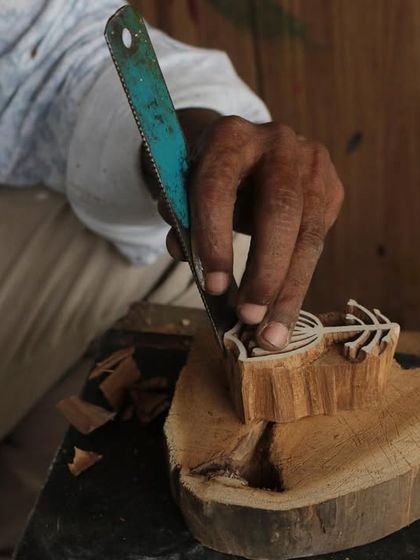 A close-up of a master carver's hands bringing a floral design to life on a teak block. This particular block was created for a collaborative workshop with the Fabric Workshop Museum in Philadelphia.