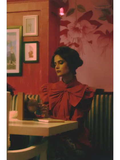 The heroine sits at a table, surrounded by framed pictures. The styling is more structured, and the setting represents the future she is imagining for herself.