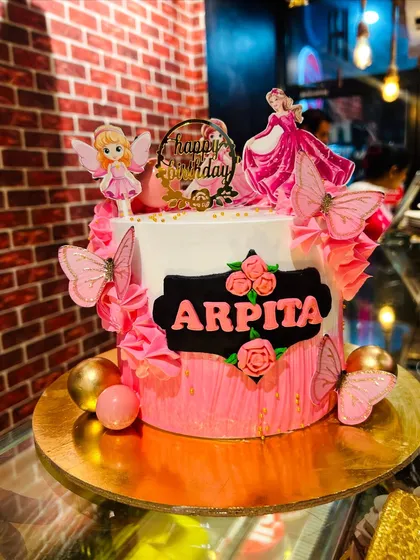 A pink and black cake decorated with fairies and butterflies for Arpita.