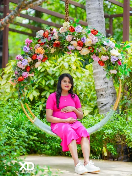 A beautiful solo portrait of the mother-to-be in a simple pink dress, seated on a floral swing.
