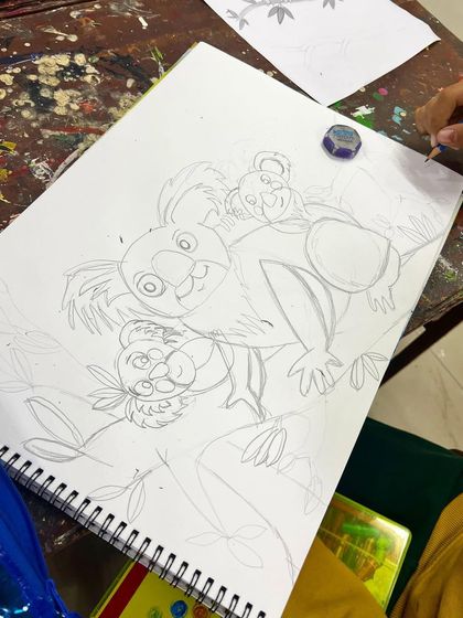 The first step: the pencil sketch. A student begins a detailed drawing of a koala family, learning about composition and proportion.