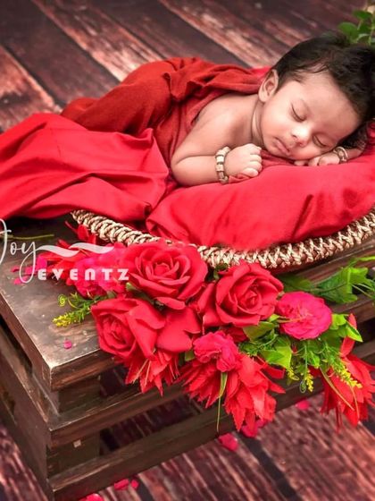 A bold and beautiful newborn photoshoot with a rustic theme. The baby is draped in rich red fabric, resting on a wooden crate adorned with vibrant red roses, creating a striking color contrast.