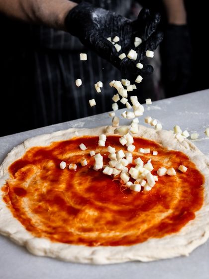 When the sauce meets its match. Cubes of fresh mozzarella are sprinkled over the tomato sauce, promising a cheesy, delicious pizza.