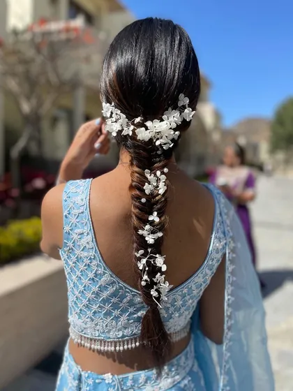A beautiful fishtail braid adorned with delicate white floral accessories. This is a dreamy and romantic look, ideal for an outdoor wedding or a pastel-themed event.