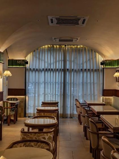 At night, warm lighting enhances the cafe's intimate ambiance, highlighting the glossy green tiles and the texture of the vaulted ceiling.
