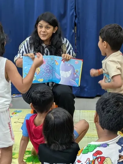 An instructor captivates the children with an illustrated storybook. You can see the excitement and curiosity on their faces as they interact with the story, shouting out answers and acting out the scenes.