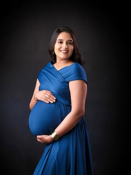 A smiling portrait in the same blue gown. This shot captures the pure joy and excitement of pregnancy, with a simple black background to make the subject pop.
