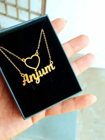 This minimalist name necklace features a single name alongside a simple, open-heart charm. It's a delicate and understated piece, perfect for everyday wear and shown here in its gift box.