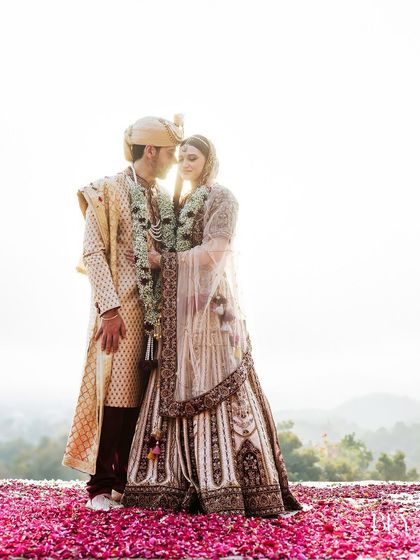 A stunning backlit portrait of a couple on their wedding day, standing on a bed of rose petals against the setting sun.