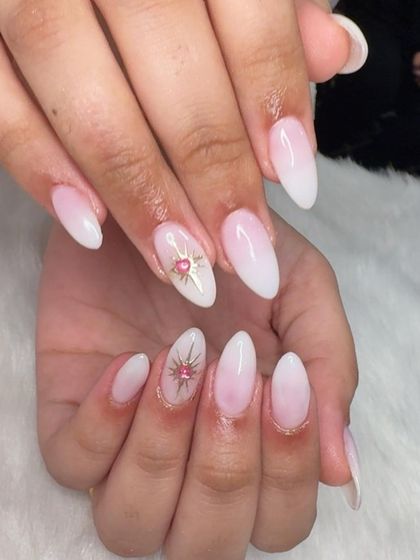 Starburst nails featuring a soft white ombré base and a gold and pink starburst accent with a rhinestone center.