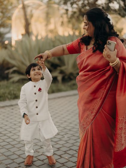 The 'bridesmaid' shares a playful moment with her son. Her handwoven red saree is both elegant and comfortable, allowing her to enjoy the festivities and her family duties with ease.