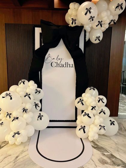 A chic black and white bow-themed entrance for 'Baby Chadha's' baby shower, featuring a giant bow and balloon clusters.