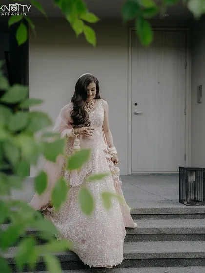 A beautiful portrait of the bride in her pastel pink lehenga, framed by lush green leaves. This shot captures her serene beauty just before she walks down the aisle at her Thailand wedding.