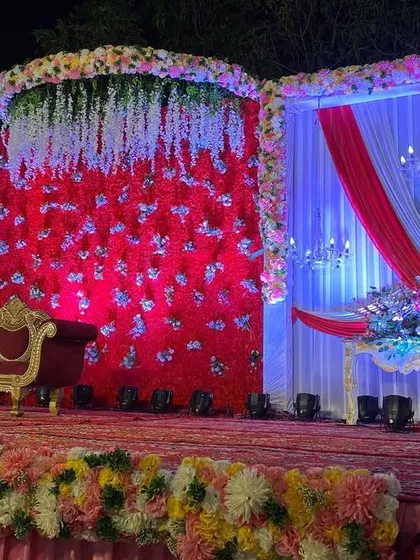 A classic reception stage with a red floral backdrop, white and red drapes, and elegant candelabras.