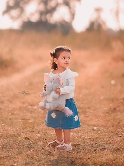 A little girl holds her stuffed elephant toy while standing in a field, with the soft, warm light creating a dreamy atmosphere.
