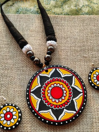 This simple and elegant necklace features a large, hand-painted mandala pendant in yellow, black, and red. It comes with matching earrings and a thick, black thread cord.
