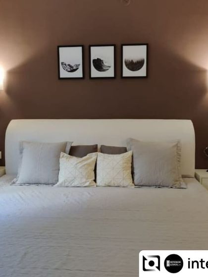 This bedroom for the seniors of the household features a muted, calming color palette. The existing wooden bed was upholstered in white and set against a dark, textured wall for a sophisticated contrast.