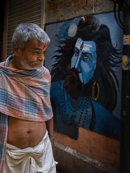 A man in Varanasi walks past a vibrant mural of Lord Shiva, the candid moment creating a visual parallel between the devotee and the deity.