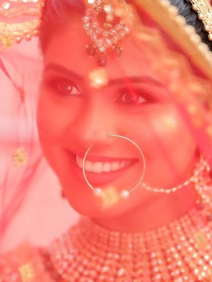 A classic bridal shot, with the bride smiling through her red veil. The soft focus and warm lighting create a dreamy and timeless portrait that highlights her joy.