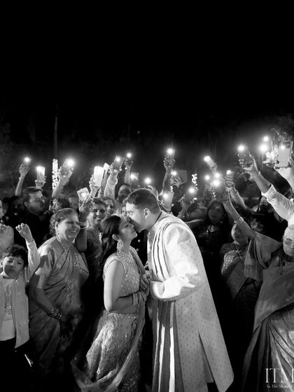 A kiss under the light of a hundred phones. This candid shot captures the couple's private moment in a public celebration, a modern take on a classic wedding memory.