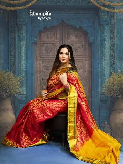 A full-length seated portrait in the stunning red and gold saree. This pose exudes grace, elegance, and a quiet confidence.