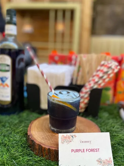 The unique Purple Forest mocktail, presented with a paper straw and a slice of orange. We focus on creative flavor combinations and beautiful presentation.