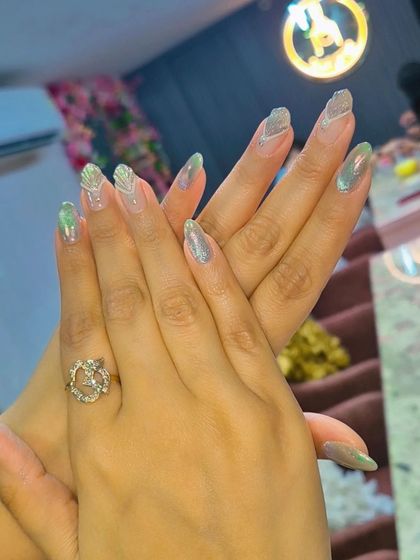 An elegant set of almond-shaped nails with a subtle green chrome finish and delicate silver line work.