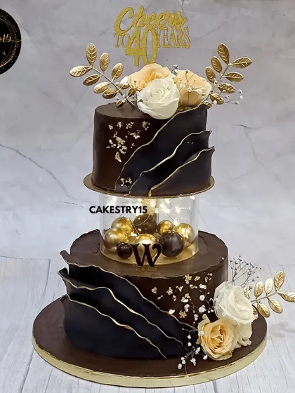 Celebrating a 40th birthday calls for something truly special. This two-tier chocolate cake features a modern, luxurious design with bold chocolate sails, an illuminated spacer, and elegant floral toppers, creating a sophisticated centerpiece for a milestone event.